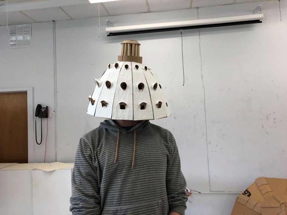 artist wearing hat made from cardboard shaped like medieval architectural dome